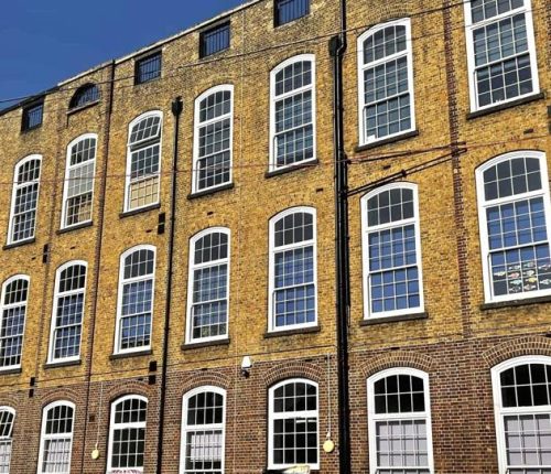 A tall brick building with large arched windows under a clear blue sky, featuring a metal fence in the foreground.