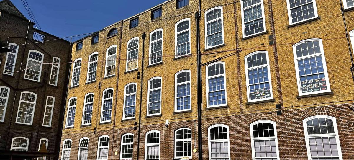 A tall brick building with large arched windows under a clear blue sky, featuring a metal fence in the foreground.